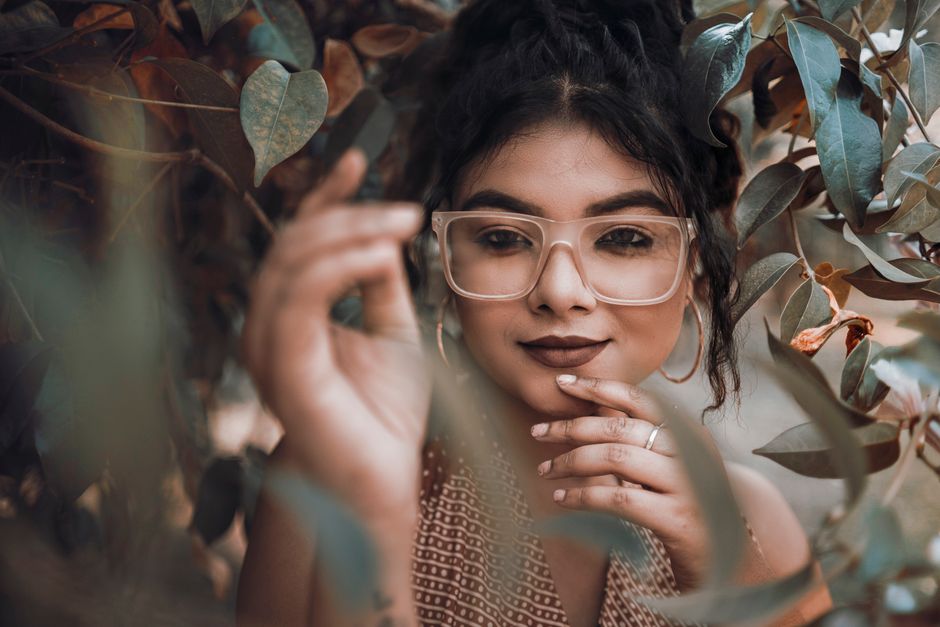 Elegant portrait of a woman with glasses surrounded by leaves, evoking a serene and natural ambiance.