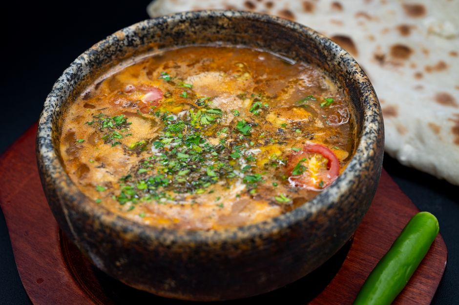 A vibrant Middle Eastern stew served in a rustic stone bowl with naan bread and green chili.