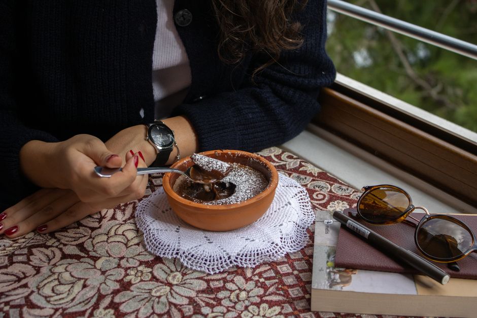 A warm moment enjoying chocolate dessert near a window with a view, featuring styled accessories.