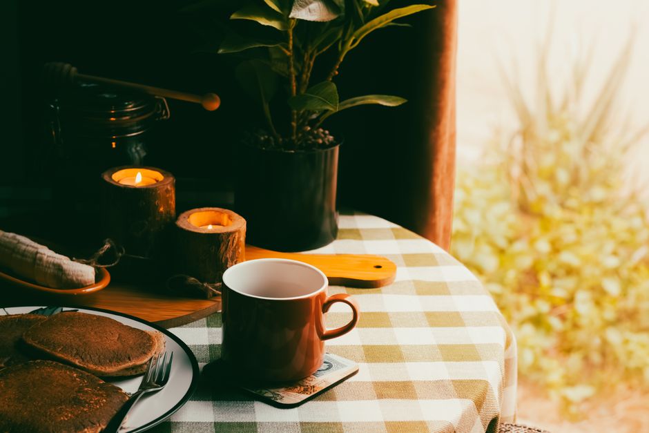 Warm and inviting breakfast setting with coffee, pancakes, and candles on a checkered tablecloth.