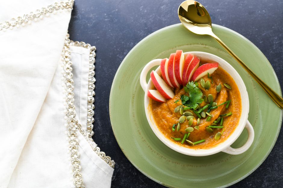 Bowl of creamy orange soup topped with apple slices and seeds