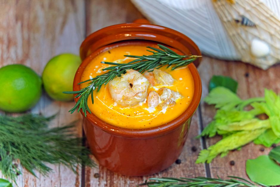 Bowl of orange squash soup garnished with rosemary and lime