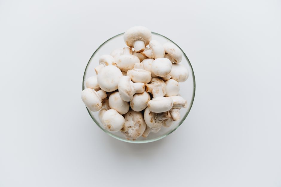 Top-down view of fresh white mushrooms in a glass bowl on a plain white background, ideal for culinary use.