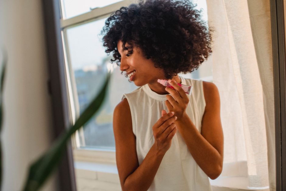 Woman applying lip balm by a bright window